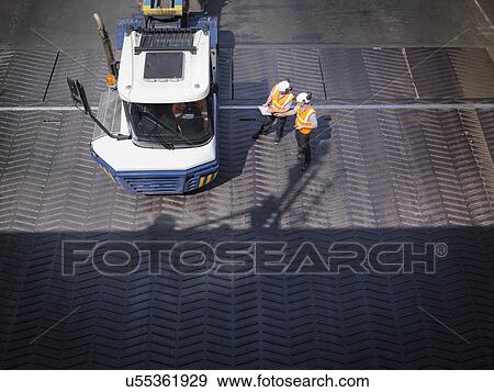 Stock Photo - Workers in discussion with truck driver on ship's ramp, elevated view. Fotosearch