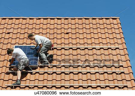 Stock Photograph - Workers installing solar panel on roof framework of new home, Netherlands. Fotosearch