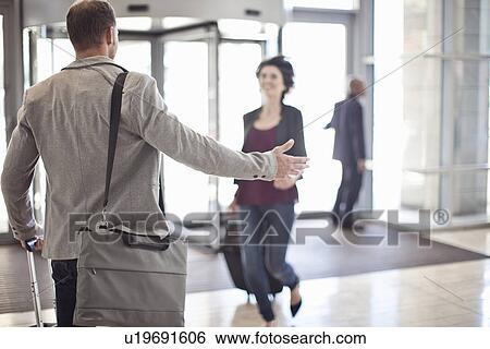 Stock Photograph - Young businessman opening arms for girlfriend in conference centre atrium. Fotosearch