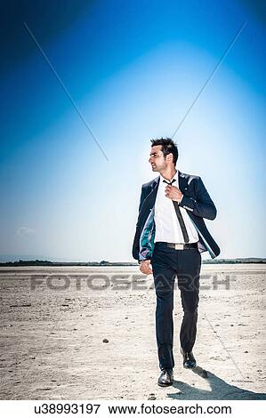 Young businessman striding through desert landscape alone View Large Photo Image Stock Photo - Young businessman striding through desert landscape alone. Fotosearch