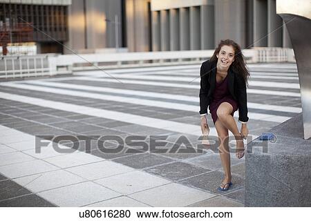 Stock Image - Young businesswoman exchanging sandals for flipflops. Fotosearch