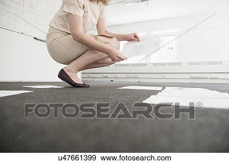 Young businesswoman organizing paperwork on empty office floor View Large Photo Image Stock Photo - Young businesswoman organizing paperwork on empty office floor. Fotosearch