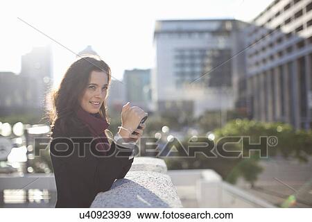Stock Photo - Young businesswoman photographing with smartphone from city rooftop. Fotosearch