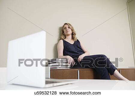 Young businesswoman sitting on cupboard in new office View Large Photo Image Stock Photo - Young businesswoman sitting on cupboard in new office. Fotosearch