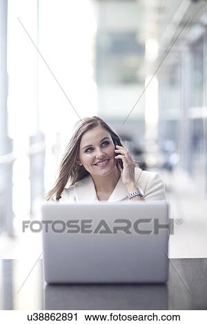 Young businesswoman using laptop and chatting on smartphone in conference centre View Large Photo Image Stock Image - Young businesswoman using laptop and chatting on smartphone in conference centre. Fotosearch