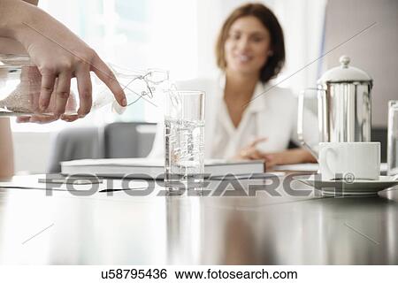 Stock Photograph - Young businesswomen pouring glass of water in conference room. Fotosearch