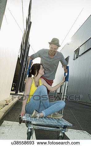 Young couple fooling around on shopping cart in street View Large Photo Image Stock Image - Young couple fooling around on shopping cart in street. Fotosearch