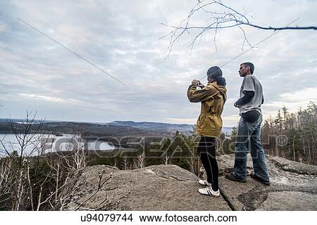 Picture - Young couple on top of rock formation photographing view. Fotosearch