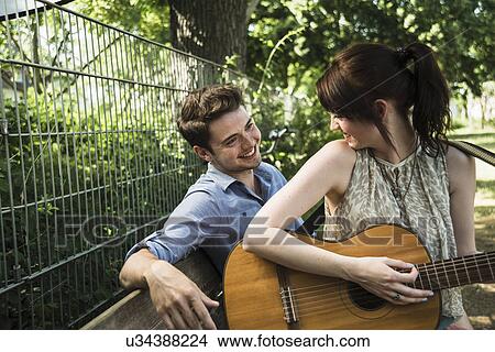 Young couple playing acoustic guitar in park View Large Photo Image Picture - Young couple playing acoustic guitar in park. Fotosearch