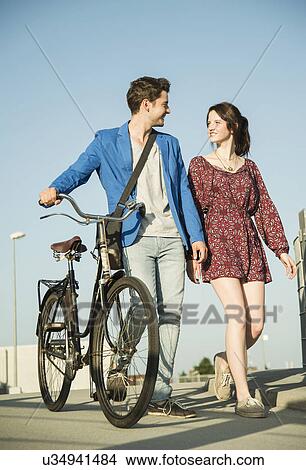 Young couple pushing bicycle along street View Large Photo Image Picture - Young couple pushing bicycle along street. Fotosearch