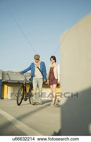 Picture - Young couple pushing bicycle along street. Fotosearch