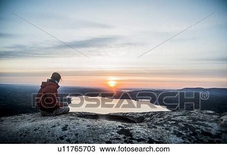 Stock Image - Young female hiker gazing at sunset over distant lake. Fotosearch