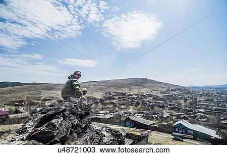Stock Image - Young female hiker looking over shoulder on top of mountain rock. Fotosearch