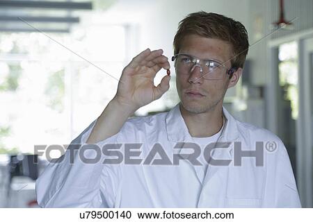 Stock Image - Young male scientist holding up pill in lab. Fotosearch