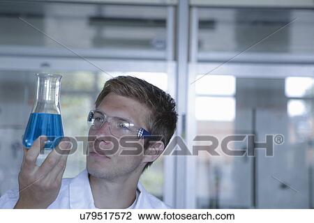 Stock Image - Young male scientist holding up erlenmeyer flask in lab. Fotosearch