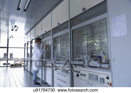 Stock Image - Young male scientist writing on fume cupboard window. Fotosearch