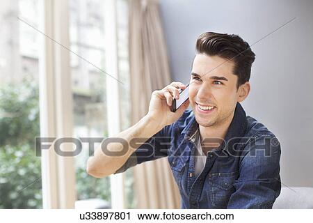 Young man chatting on smartphone in living room View Large Photo Image Stock Image - Young man chatting on smartphone in living room. Fotosearch
