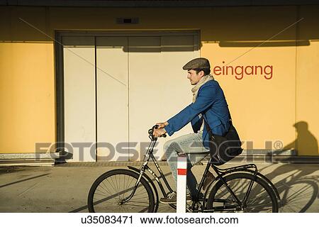 Young man cycling along urban street View Large Photo Image Stock Image - Young man cycling along urban street. Fotosearch
