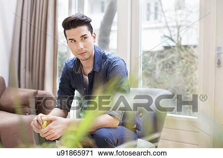 Stock Image - Young man having coffee in living room. Fotosearch