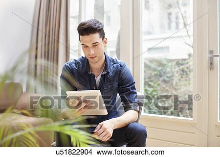 Picture - Young man looking at digital tablet in sitting room. Fotosearch