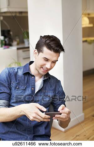 Young man looking at smartphone in kitchen View Large Photo Image Stock Photograph - Young man looking at smartphone in kitchen. Fotosearch