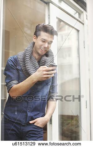 Stock Photo - Young man texting on smartphone behind patio glass. Fotosearch