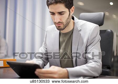 Young man using digital tablet in office View Large Photo Image Stock Image - Young man using digital tablet in office. Fotosearch