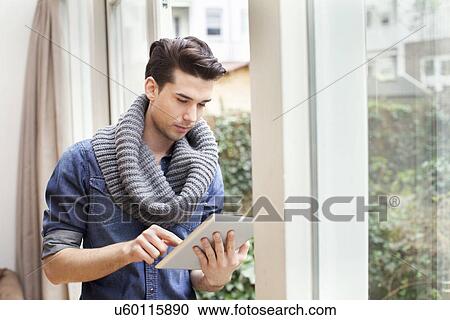 Stock Image - Young man using digital tablet in living room. Fotosearch