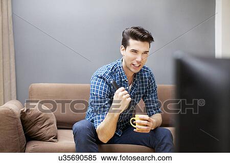 Young man watching TV in living room View Large Photo Image Stock Photography - Young man watching TV in living room. Fotosearch