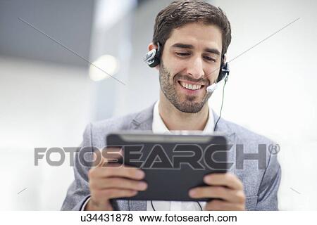 Young man wearing headset using digital tablet View Large Photo Image Stock Photo - Young man wearing headset using digital tablet. Fotosearch