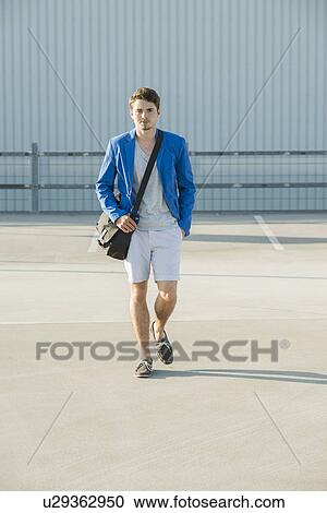 Young man with shoulder bag strolling across empty parking lot View Large Photo Image Stock Image - Young man with shoulder bag strolling across empty parking lot. Fotosearch