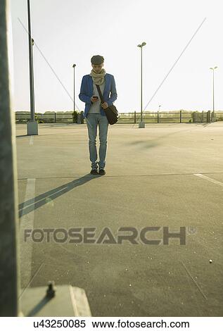 Young man with smartphone strolling across empty parking lot View Large Photo Image Stock Photography - Young man with smartphone strolling across empty parking lot. Fotosearch