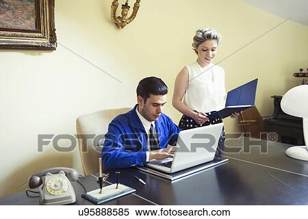 Stock Photography - Young vintage couple at desk with files and laptop. Fotosearch