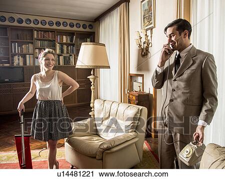 Stock Image - Young vintage couple in sitting room with vintage telephone and vacuum cleaner. Fotosearch