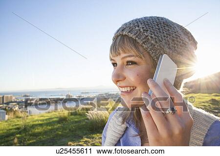 Stock Image - Young woman chatting on smartphone, view of harbour in background, Cape Town, South Africa. Fotosearch