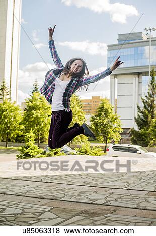 Stock Photo - Young woman jumping mid air in city. Fotosearch