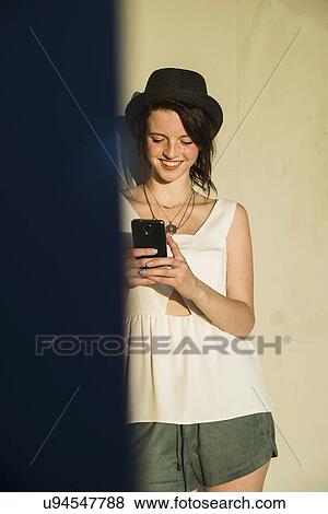 Young woman leaning against wall reading text on smartphone View Large Photo Image Stock Photo - Young woman leaning against wall reading text on smartphone. Fotosearch