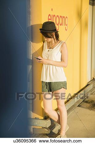 Young woman leaning against wall texting on smartphone View Large Photo Image Stock Photograph - Young woman leaning against wall texting on smartphone. Fotosearch