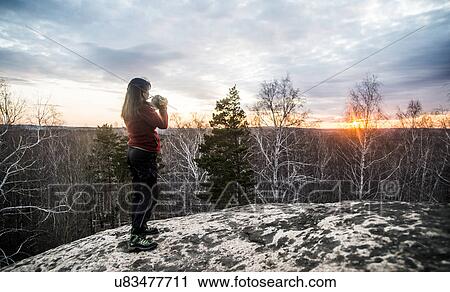 Young woman on top of rock photographing sunset View Large Photo Image Stock Image - Young woman on top of rock photographing sunset. Fotosearch
