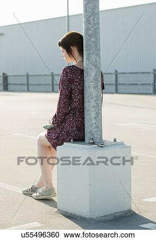 Young woman sitting leaning against lamp post in empty parking lot View Large Photo Image Stock Image - Young woman sitting leaning against lamp post in empty parking lot. Fotosearch