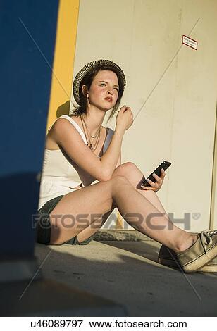 Young woman sitting outside building with smartphone View Large Photo Image Stock Photo - Young woman sitting outside building with smartphone. Fotosearch