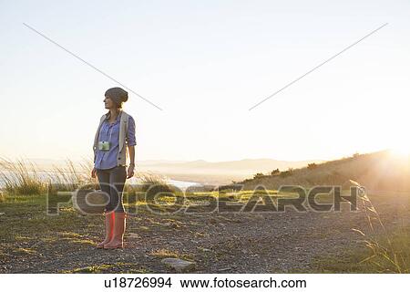 Picture - Young woman standing on hill at sunset. Fotosearch