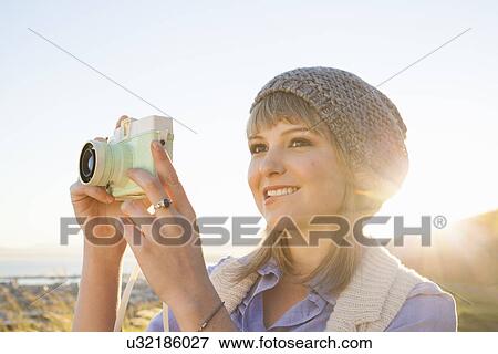 Stock Photo - Young woman taking photograph with camera at sunset. Fotosearch