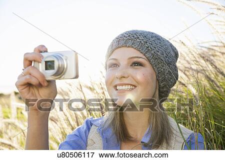 Stock Photo - Young woman taking photograph with camera in fields. Fotosearch