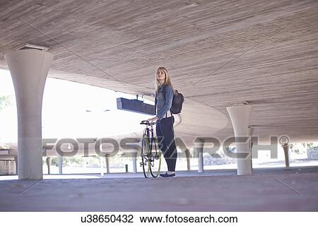Stock Image - Young woman waiting with bicycle in city underpass. Fotosearch