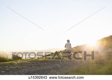 Young woman walking on hill at sunset View Large Photo Image Stock Image - Young woman walking on hill at sunset. Fotosearch