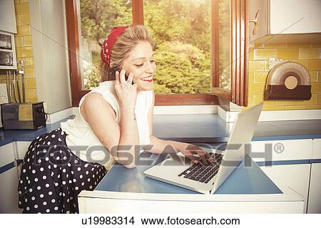 Picture - Young woman wearing vintage clothes using laptop and cellphone. Fotosearch