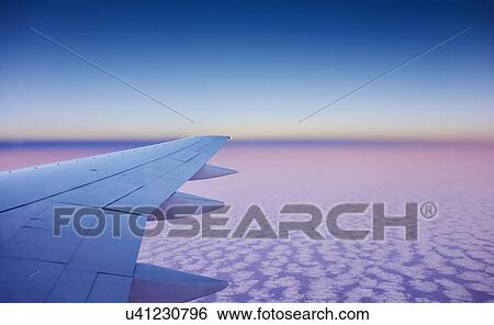 Stock Photograph - Atmospheric elevated view of airplane wing above the clouds. Fotosearch