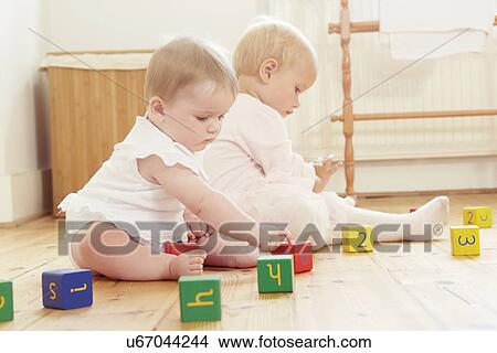 Picture - Baby sisters playing on floor with building blocks. Fotosearch