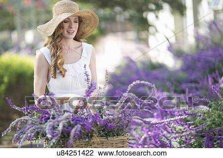 Stock Image - Beautiful young woman in garden looking at purple flowers. Fotosearch